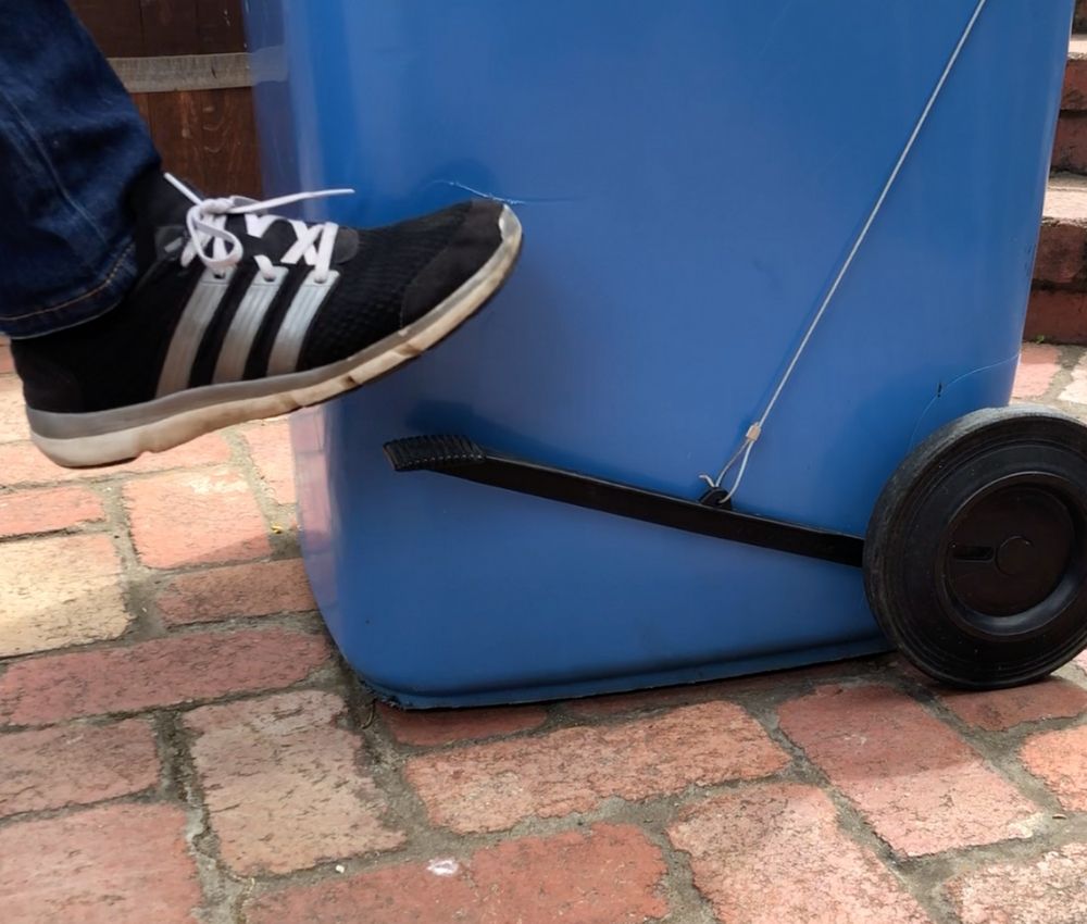 Foot pressing the BLOP bin lid opener pedal attached to the side of a blue wheelie bin