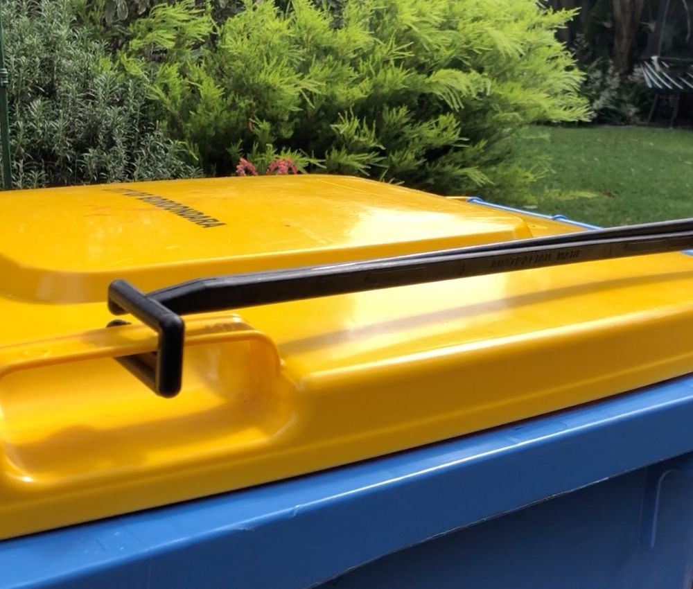 Close-up of the BLOP bin lid opener lifting arm attached to the yellow lid of a blue wheelie bin