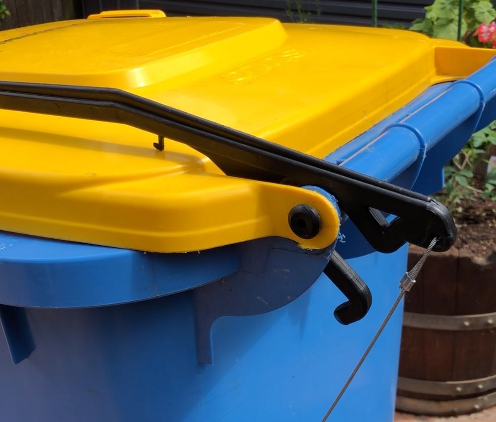 Close-up of the BLOP bin lid opener lifting arm and connecting cable fitted to a blue wheelie bin with a yellow lid