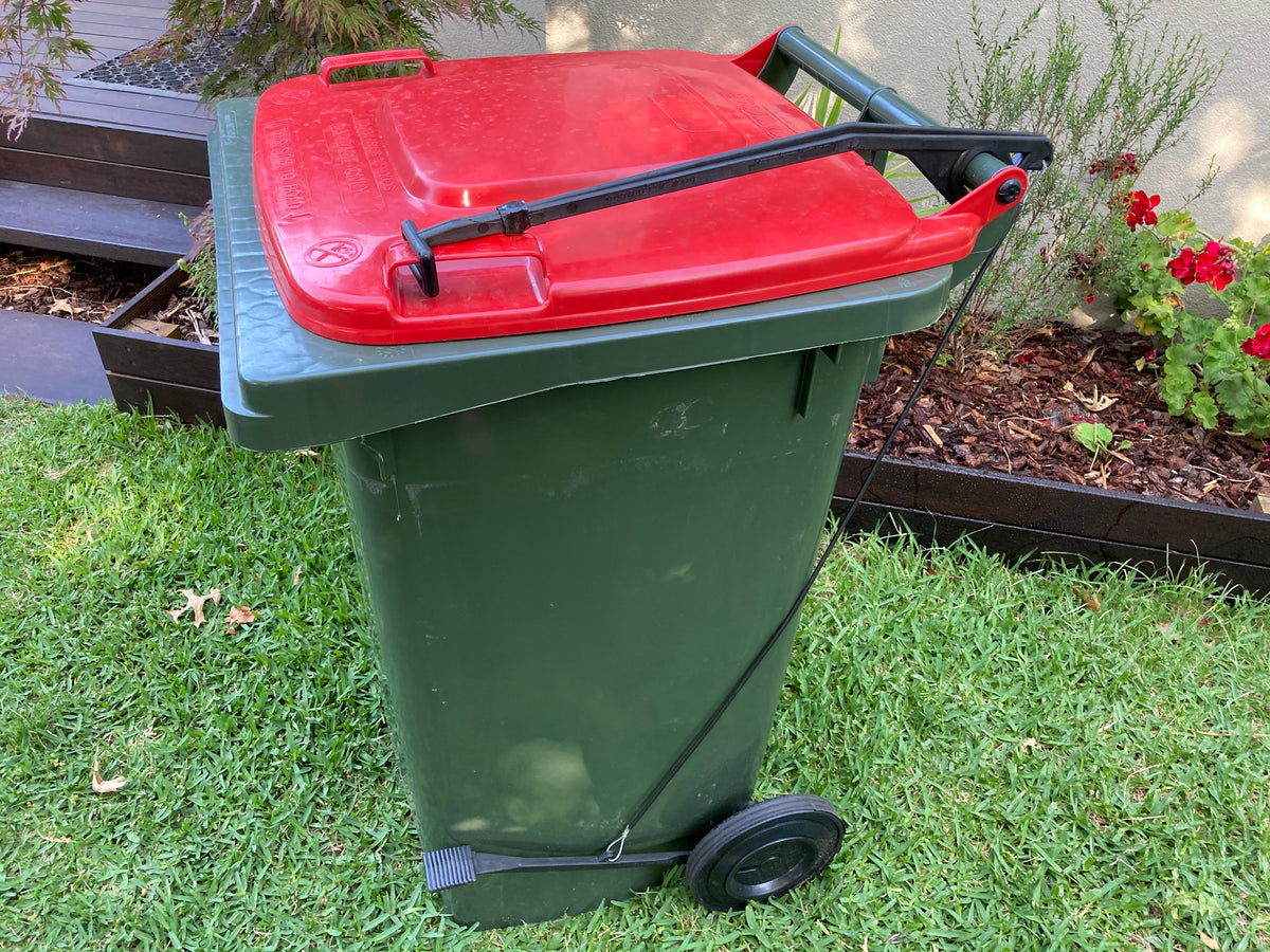 BLOP foot-operated bin lid opener installed on a green wheelie bin with a closed lid, showing the pedal, cable and lifting arm
