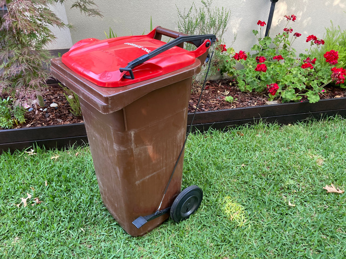 BLOP foot-operated bin lid opener fitted to a brown wheelie bin with a red lid, showing the pedal, cable and lifting arm
